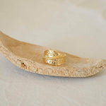 An 18K gold plated stainless steel asymmetric ring with a textured surface, displayed on a natural stone surface.