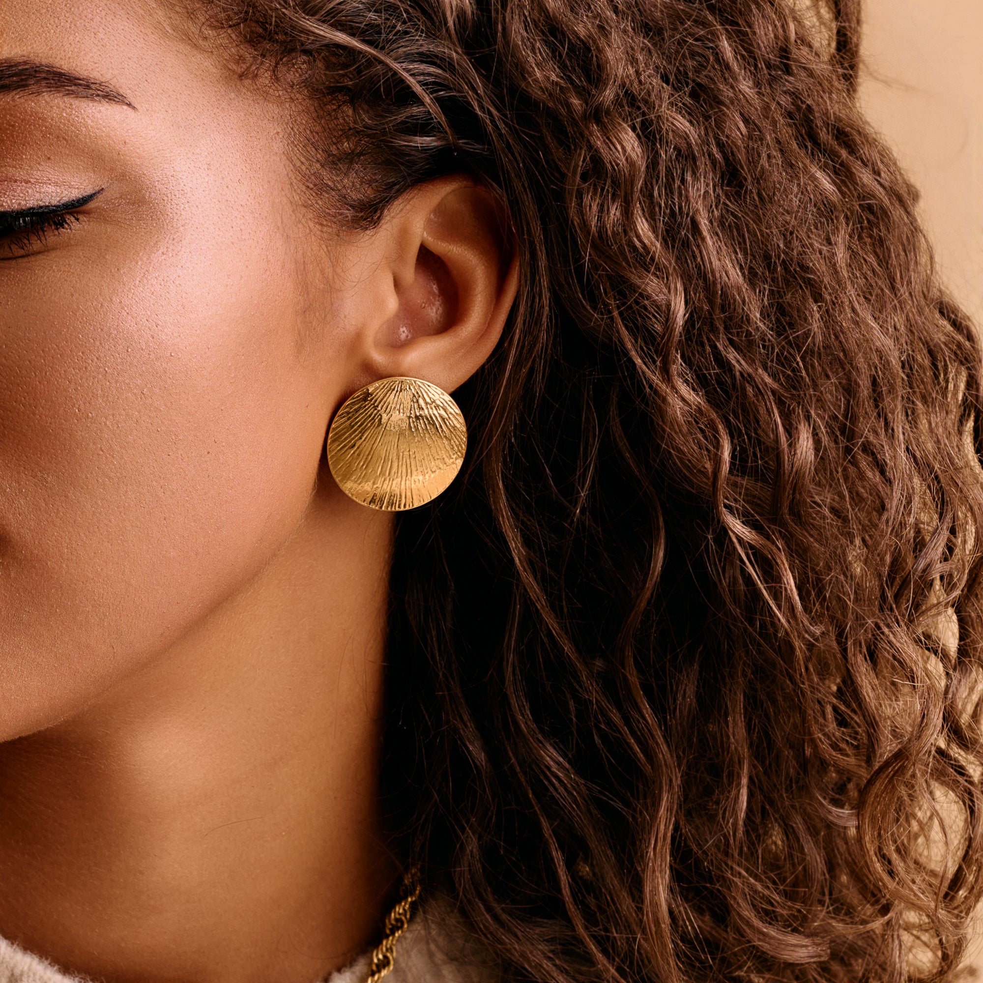 A woman wearing large gold disc earrings with a hammered design.