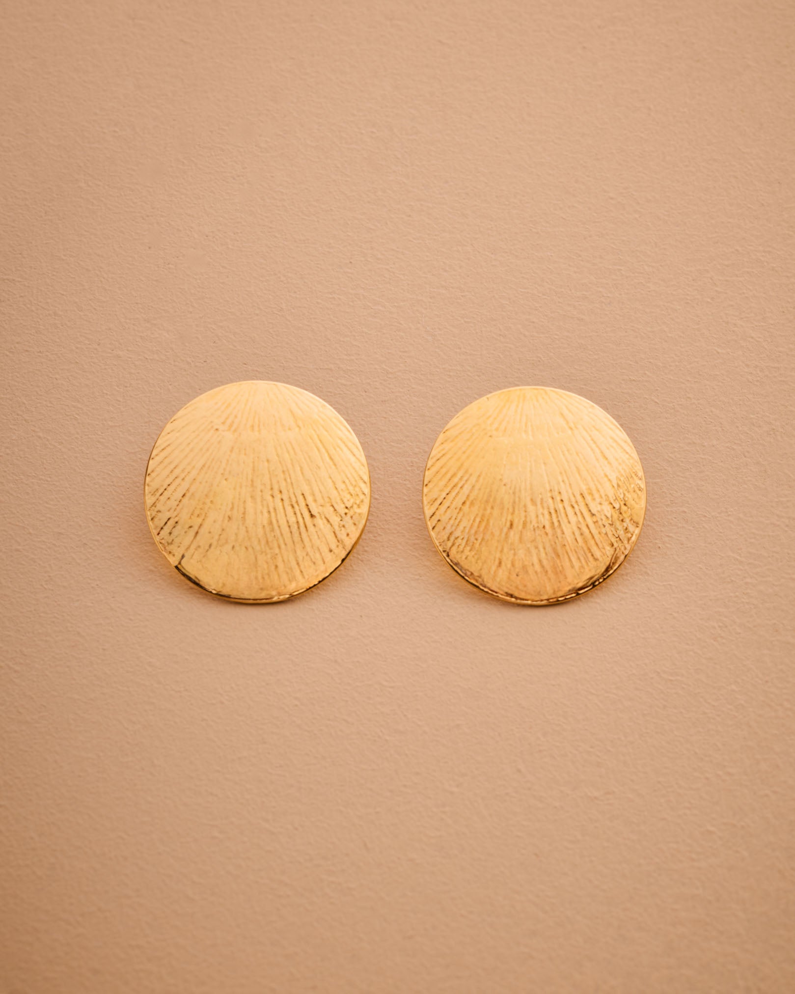 Pair of gold round earrings on a beige background