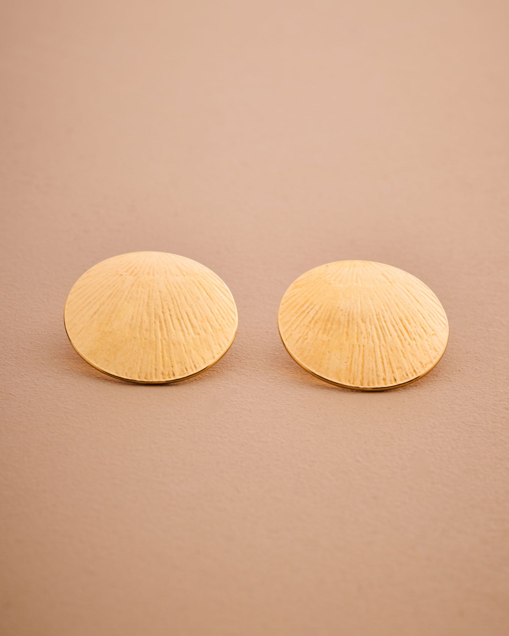 Pair of gold shell-shaped earrings on a beige background
