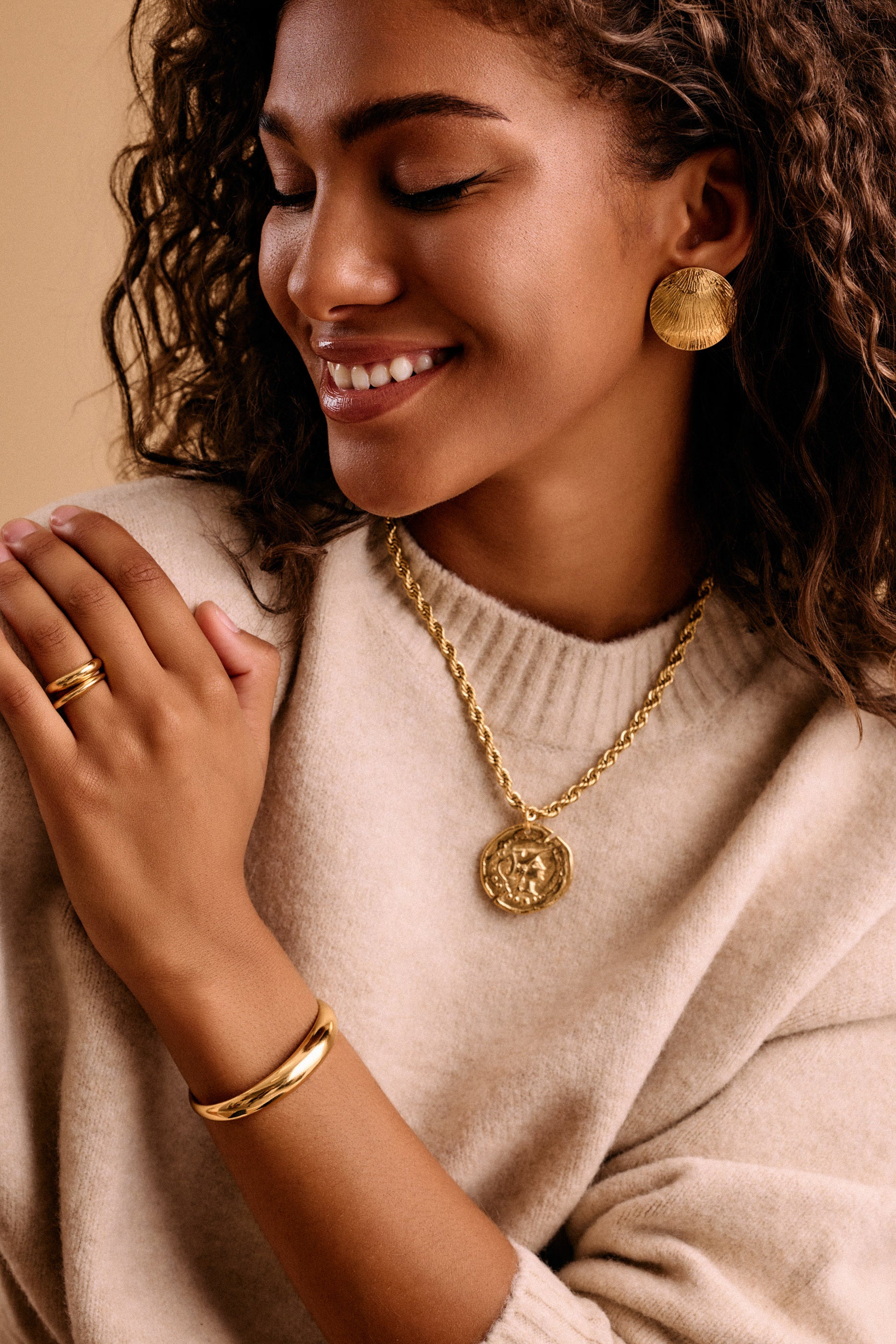 Woman wearing large gold disc earrings and achunky gold pendant with a neutral background