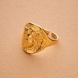 Gold ring with a face design on a beige background