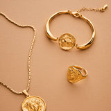 Gold necklace, bracelet, and ring set on a beige background