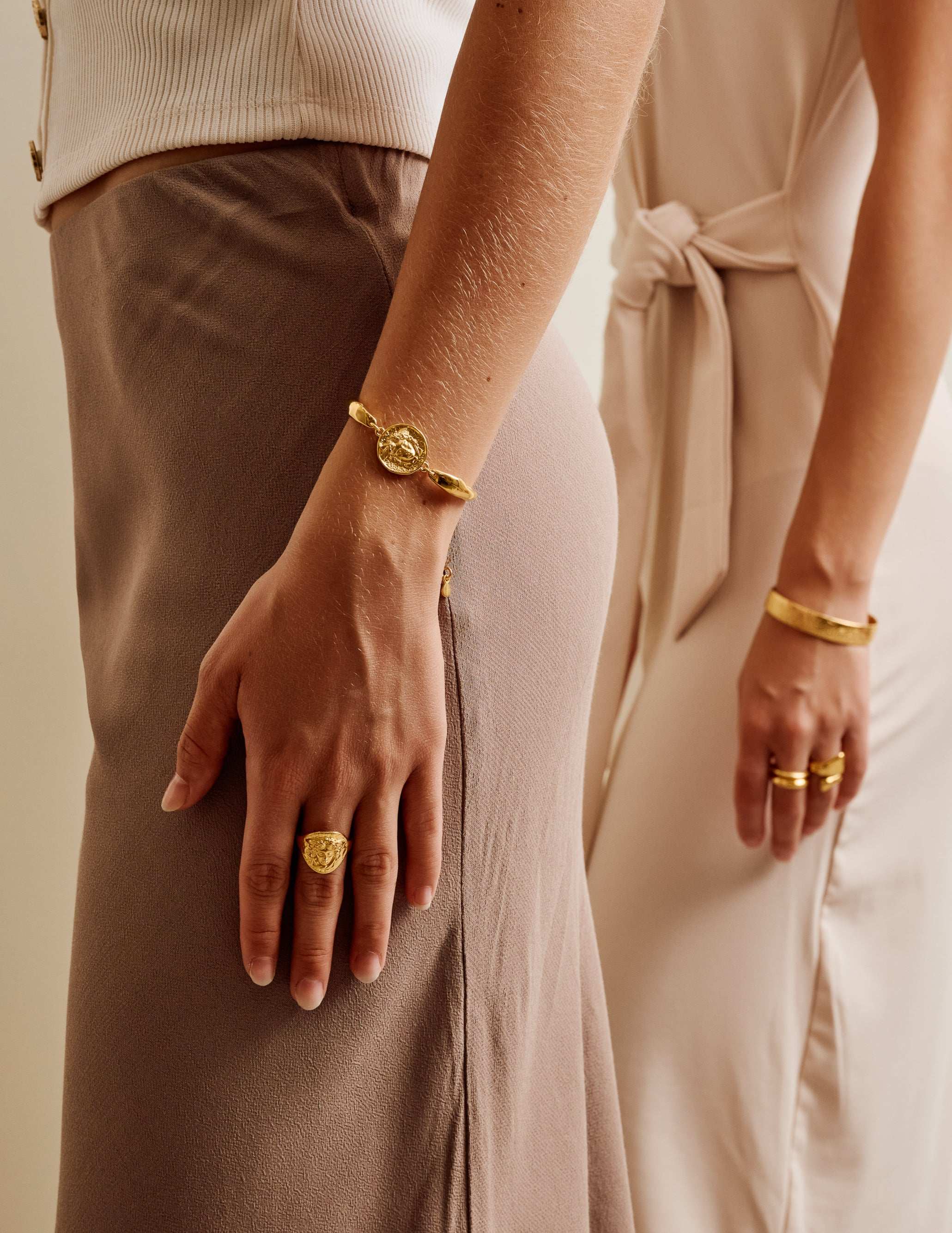 Two people holding hands with gold jewelry against a neutral background