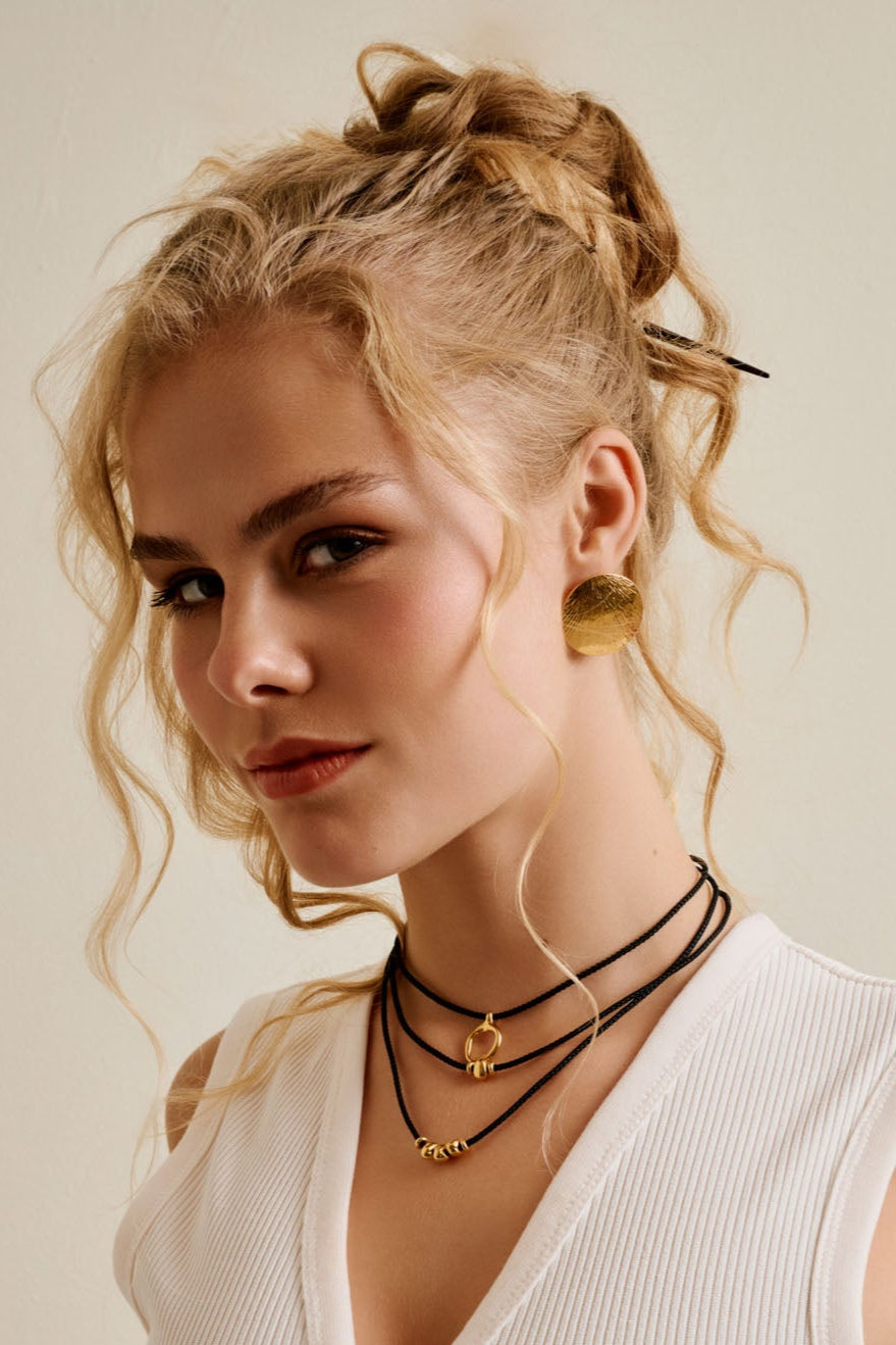 Woman wearing a white sleeveless top with gold buttons against a neutral background