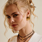 Woman wearing a white sleeveless top with gold buttons against a neutral background