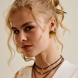 Woman wearing a white sleeveless top with gold buttons against a neutral background