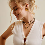 Woman wearing a white sleeveless top with gold buttons and necklaces, against a plain background