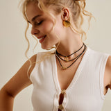 Woman wearing a white sleeveless top with gold buttons and necklaces, against a plain background