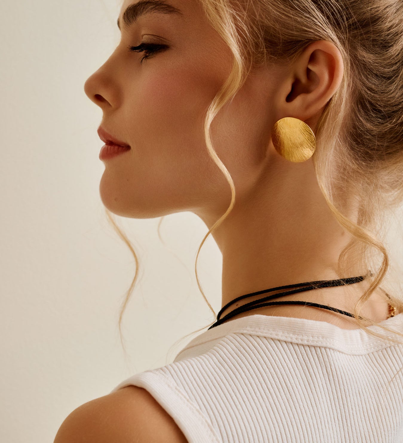 Woman wearing large gold disc earrings with a neutral background
