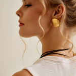 Woman wearing large gold disc earrings with a neutral background