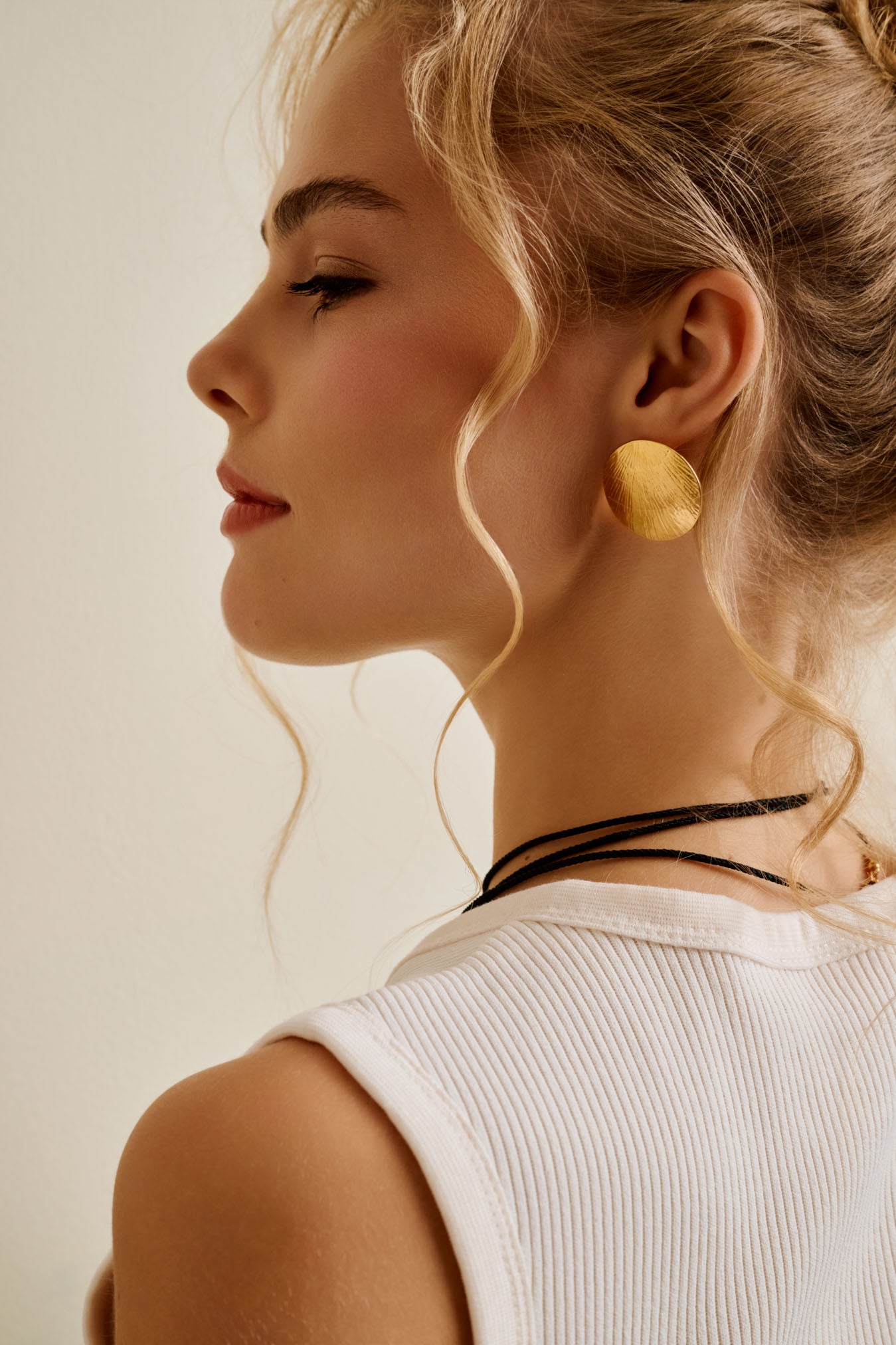 Woman wearing large gold disc earrings with a neutral background
